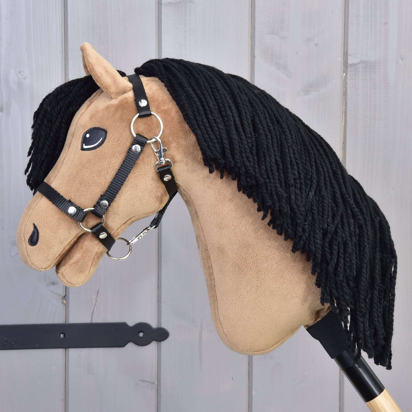 Hobby Horse Samantha s černou ohlávkou od Hobby Horse LarDen má béžový obličej, černou přízovou hřívu, vyšívané detaily a černou ohlávku, na světlém dřevěném pozadí.