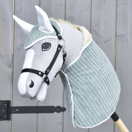 Set Manchester Little Green od Hobby Horse LarDen se šedo-bílým Hobby Horse s měkkou látkovou hlavou, černou uzdečkou, čabrakou a světle modrozeleným krytem krku na dřevěné tyči, zobrazený před dřevěným plotem.