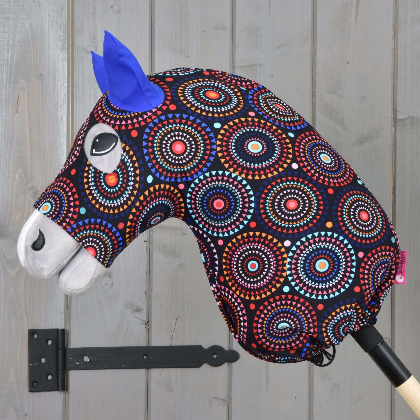 Výrazný Hobby Horse se vzorovanou hlavou z lycry, modrýma plstěnýma ušima a bílými detaily na dřevěné tyči – perfektně sladěný s Hobby Horse LarDen „Hobby Horse Protective Suit Alice (Lycra)“.
