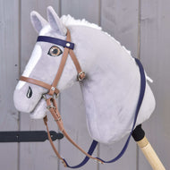 Plyšový Hobby Horse LarDen se světle šedou srstí, bílou hřívou a lysinou, s Kompletní uzdečka s nánosníkem Brown Purple, nasazený na dřevěné tyči na šedém dřevěném pozadí.