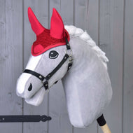 Šedý Hobby Horse od Hobby Horse LarDen s bílou hřívou, černou uzdečkou a čabrakou Čabraka háčkovaná červená pro ochranu proti mouchám, před světlým dřevěným pozadím.