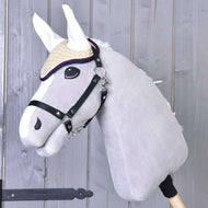 Šedý plyšový Hobby Horse od Hobby Horse LarDen s červenou háčkovanou čabrakou Nicol, uzdečkou a slaměným kloboukem, nasazený na dřevěné tyči a zobrazený před pozadím z dřevěných prken.
