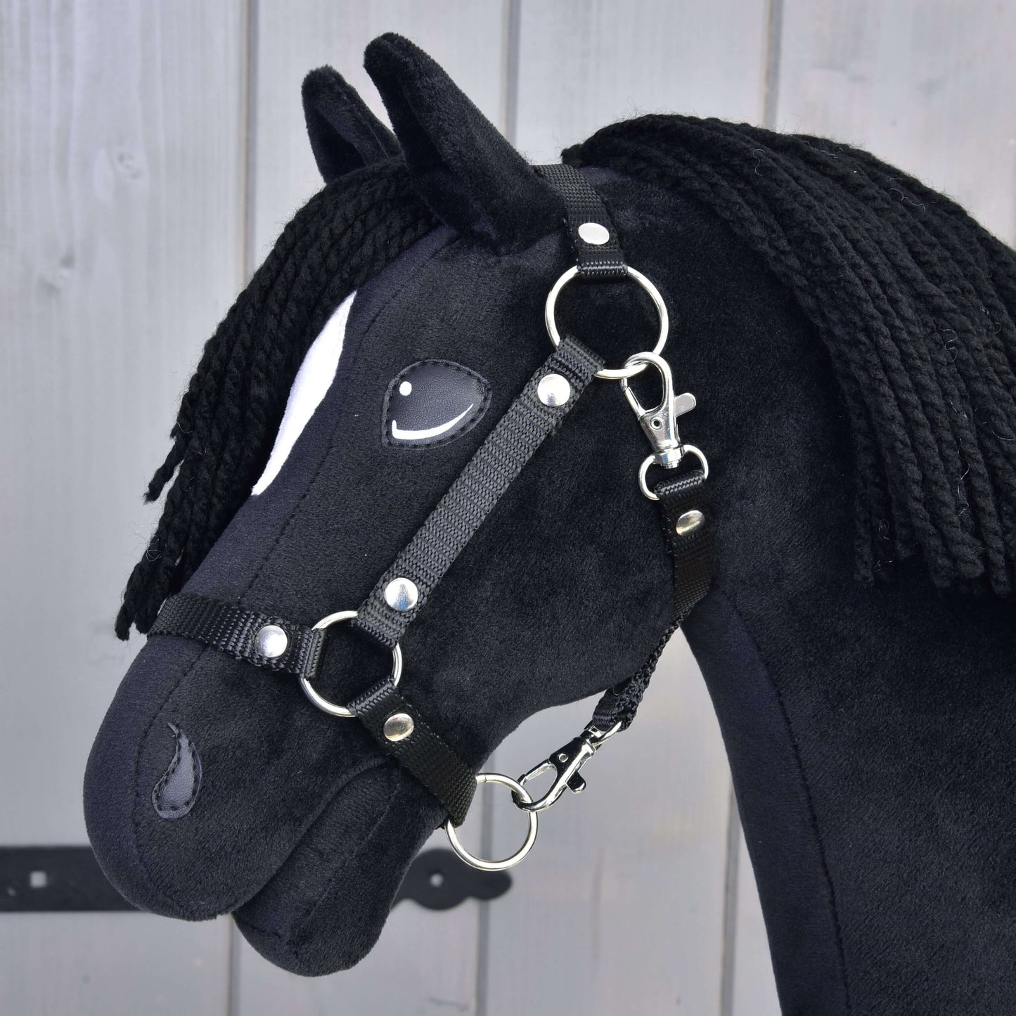 Hobby Horse Cloony s černou ohlávkou od Hobby Horse LarDen, černý látkový kůň ve stylu hřebce American Quarter Horse, s bílou skvrnou u oka, černou přízovou hřívou, vyfotografovaný na světlém dřevě.