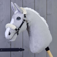 Černá ohlávka z koženky s beránkem od Hobby Horse LarDen na šedém plyšovém koni s bílou hřívou a černou ohlávkou, na dřevěné tyči, na pozadí dřevěných panelů.