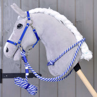 Plyšový šedý Hobby Horse od Hobby Horse LarDen se sadou Set Start modrý (ohlávka + vodítko + otěže + nákrčník), s modro-bílým vodítkem na dřevěné tyči, stojí před šedou dřevěnou stěnou.