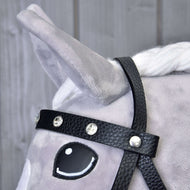 Detail hlavy šedého plyšového koně s Kompletní uzdečkou s kamínky z eko kůže od Hobby Horse LarDen. Kůň má bílou hřívu, vztyčené ucho, oko v kresleném stylu a v pozadí jsou světlé dřevěné desky.