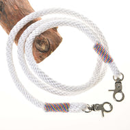 Otěže bílé od Hobby Horse LarDen s kovovými karabinami na obou koncích a duhově barevnou nití u každé karabiny, stočené na dřevě na bílém pozadí, připomínající kvalitní otěže k bezudidlové uzdečce.