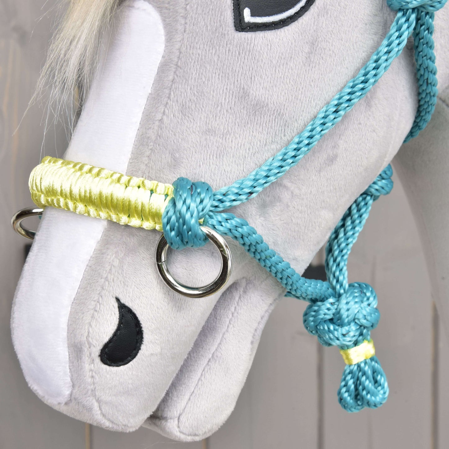 Detail šedého plyšového Hobby Horse od Hobby Horse LarDen s Parelka Tyrkys a uzdečkou, černě vyšívanýma očima a nozdrami a hřívou z bílé příze.