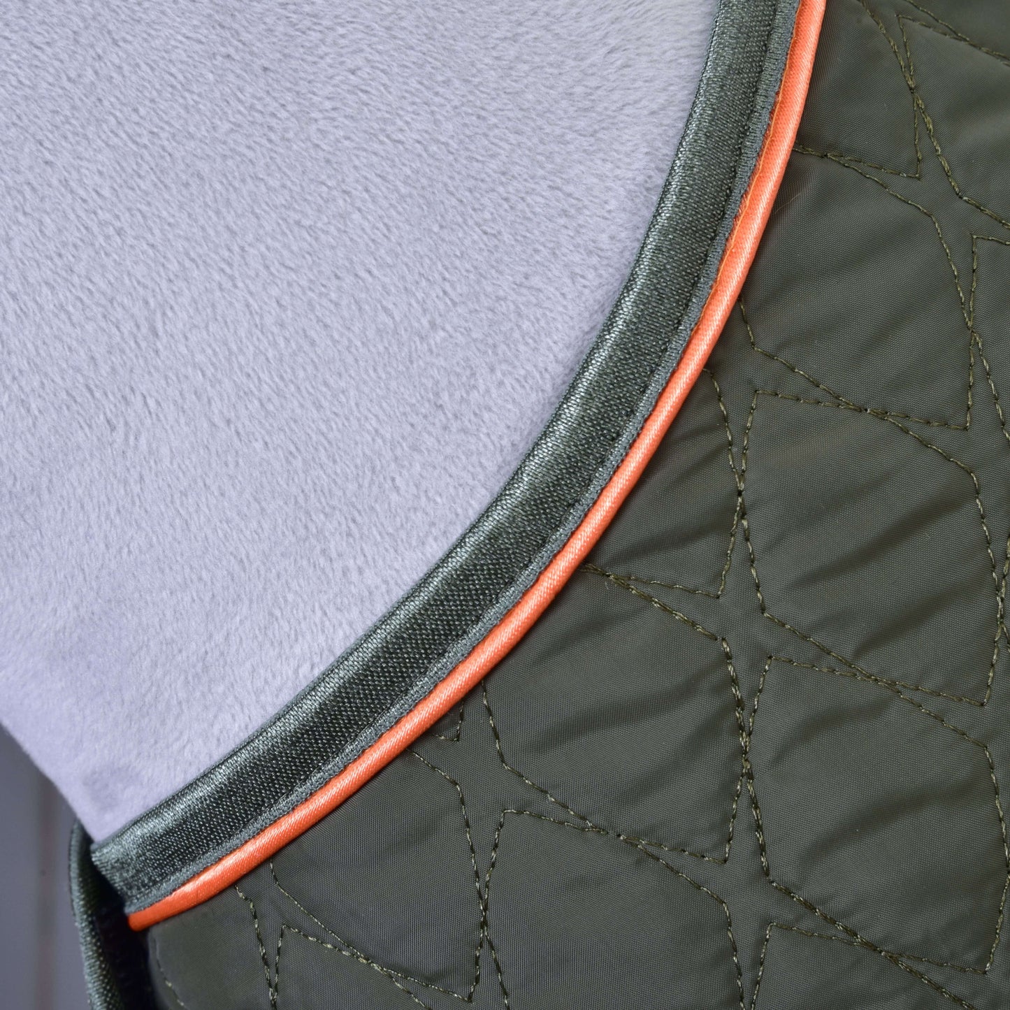 Deka Sport od Hobby Horse LarDen, prošívaná zelená ochranná koňská deka s oranžovým lemováním a viditelným prošíváním, zobrazená zblízka na měkkém světle šedém strukturovaném povrchu.