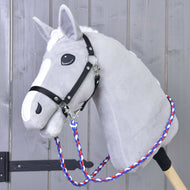 Hobby Horse LarDen Otěže Flag CZ na šedém plyšovém Hobby Horse s bílou hřívou, černou uzdečkou, ručně vyráběnými otěžemi a modro-červeno-bílým pleteným vodítkem z polypropylenového lana, na dřevěné tyči před šedým dřevěným pozadím.