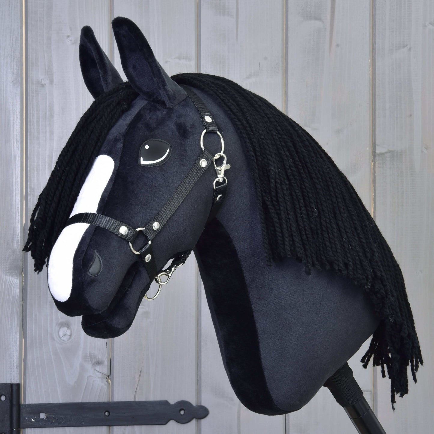 Hobby Horse Freya s černou ohlávkou od Hobby Horse LarDen má černou látku, bílý nosní pruh a dlouhou černou přízovou hřívu inspirovanou plemenem Irish Cob, zobrazená na světlém dřevěném pozadí.