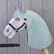 Hobby Horse LarDen „Pláštěnka Greeny“ na plyšovém koni oblečeném v zelené pláštěnce se vzorem kapek vody a s černou uzdečkou, stojícím u šedé dřevěné stěny. Vyšívané detaily a vztyčené uši nabízejí zábavnou hru za každého počasí.
