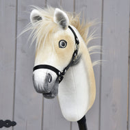 Hobby Horse Honey Pearl s černou ohlávkou - velikost S od Hobby Horse LarDen, plyšový Hobby Horse ve stylu oldenburského koně s béžovou hřívou, šedým čenichem a černou ohlávkou, nasazený na tyči před šedou dřevěnou stěnou.