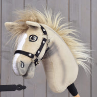 A person holds the Hobby Horse LarDen “Hobby Horse Ivory Dream with Black Halter” in size XS, featuring a light tan coat, white facial markings, a fluffy mane, and a black halter, against a wooden background.