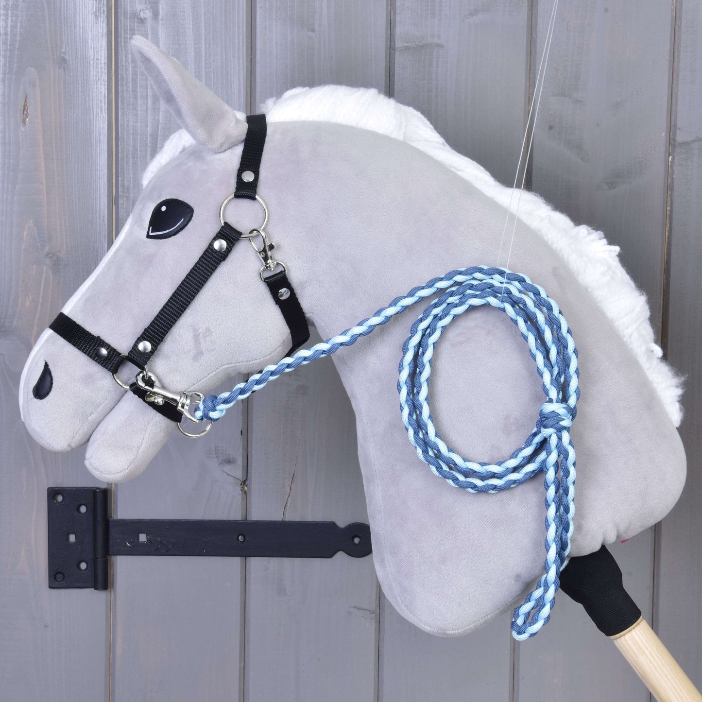 Hobby Horse - pletené vodítko Double Blue od Hobby Horse LarDen na šedém plyšovém koni s černou uzdečkou a modrým ručně pleteným vodítkem s prémiovou karabinou, vystavené před dřevěnou stěnou.