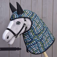 Plyšový Hobby Horse LarDen s černou ohlávkou má na sobě Pláštěnku Lara s kapucí a ušima v modrém, zeleném, bílém a černém kohoutím vzoru a je vyfocen před dřevěným plotem.