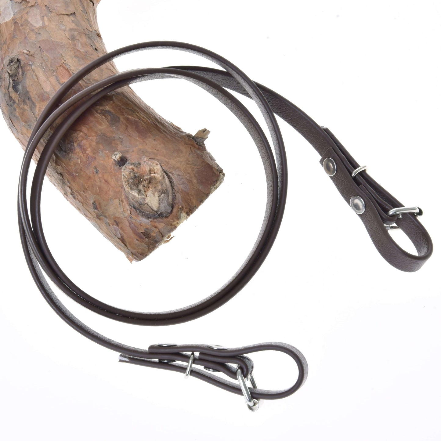 Otěže Light brown od Hobby Horse LarDen jsou přehozené přes texturovanou větev stromu na bílém pozadí a zvýrazňují svůj stylový kožený vzhled a kovové kování připomínající otěže k bezudidlové uzdečce.
