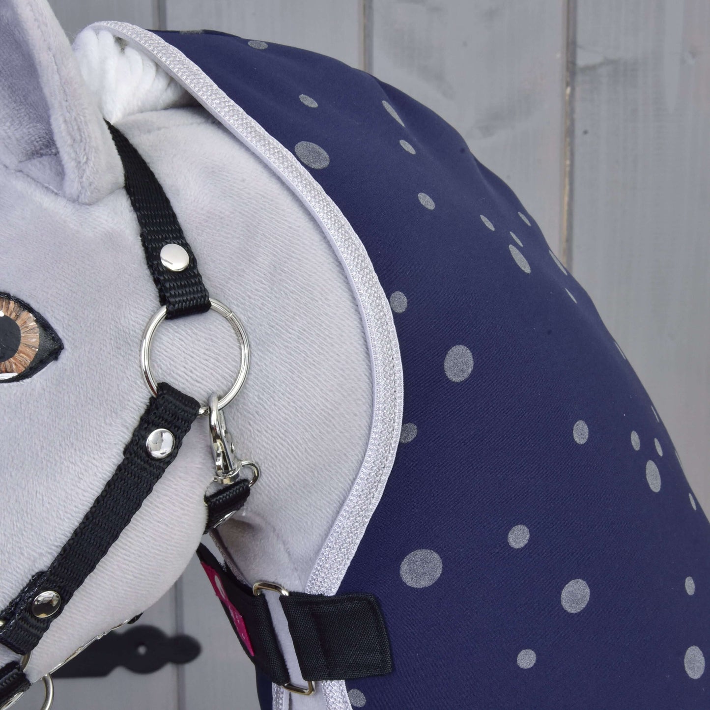 Detail plyšového koně s Dekou stájovou Night Sky od Hobby Horse LarDen – tmavě modrou se světle šedými puntíky – a černou ohlávkou, na světle šedém dřevěném pozadí.