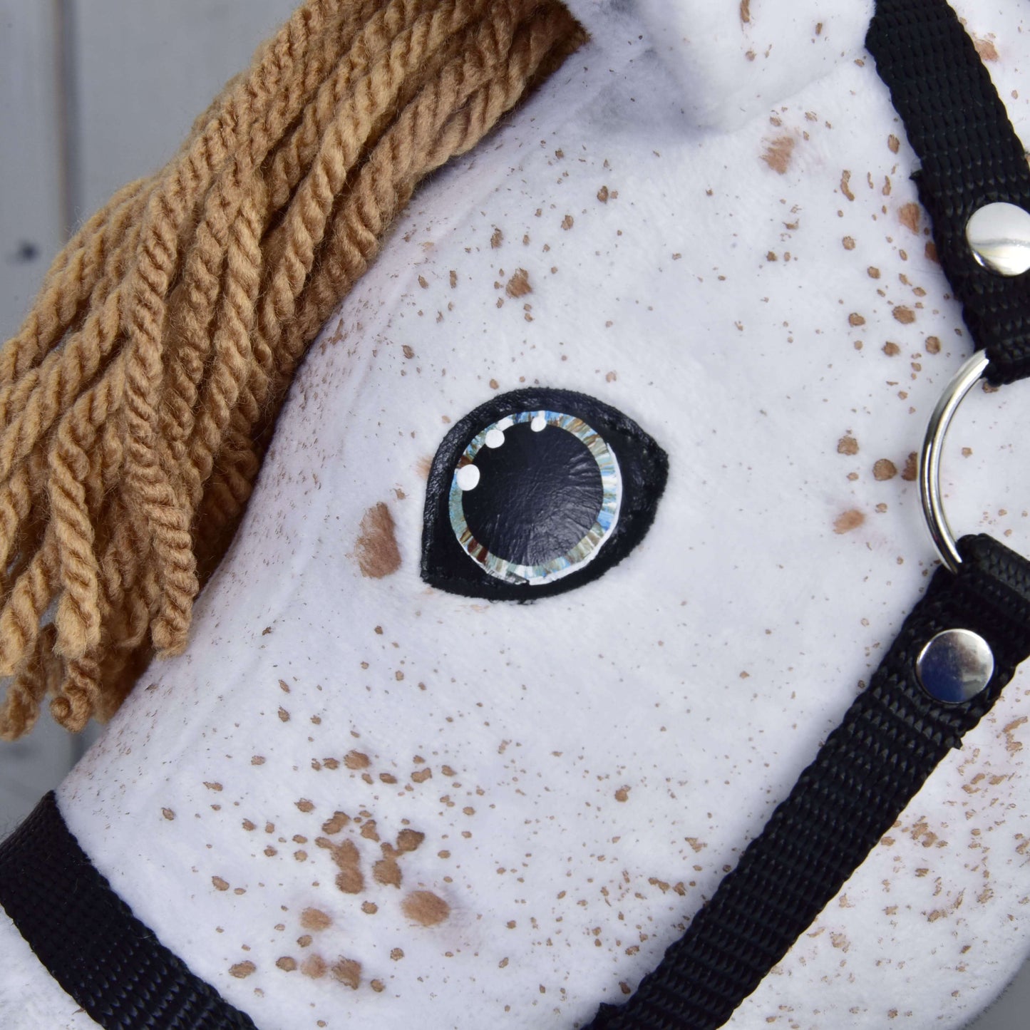 Detail Hobby Horse Rufus s černou ohlávkou od Hobby Horse LarDen: bílý Hobby Horse Appaloosa s hnědou hřívou z příze, černou ohlávkou, černobílým šitým okem a plyšovou látkou s hnědými skvrnami jako u hřebce Appaloosa.