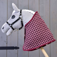 Hobby Horse LarDen "Set slavnostní Bordeaux" s šedým plyšovým Hobby Horse s černou uzdečkou a vínovo-růžovou dekou se vzorem kohoutí stopy, nasazeným na dřevěné tyči na pozadí šedých dřevěných prken.