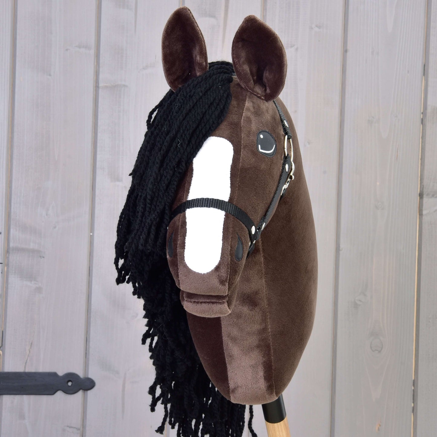 Hobby Horse Sisi s černou ohlávkou od Hobby Horse LarDen, s tmavě hnědou hlavou, bílým znakem na čenichu, černou přízovou hřívou a uzdečkou, zachycující eleganci hanoverského sportovního koně na světle dřevěném pozadí.