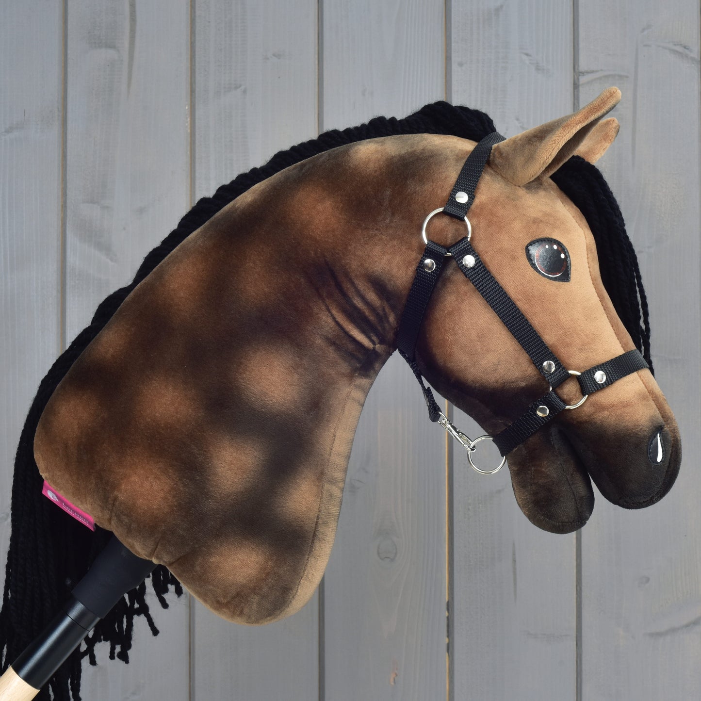 Hobby Horse Stormy s černou ohlávkou od Hobby Horse LarDen, plyšový šimlový Hobby Horse s hnědočernou hřívou, před dřevěným panelovým pozadím.
