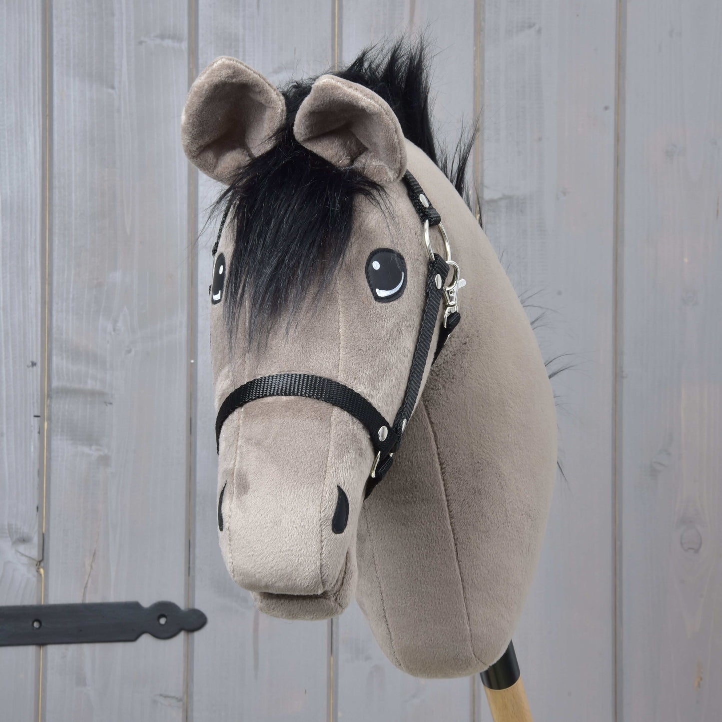 Hobby Horse Thor s černou ohlávkou od Hobby Horse LarDen, s měkkou šedou hlavou, černou hřívou a postrojem na dřevěné tyči, na pozadí světlých dřevěných panelů.