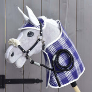 Set Cube (čabraka, deka, ohlávka s beránkem, vodítko) od Hobby Horse LarDen s dekou, čabrakou, vodítkem a ohlávkou s beránkem, vystavený na dřevěné stěně u černého pantu brány. Doplňky zdůrazňují kvalitu a kouzlo produktů Hobby Horse LarDen.
