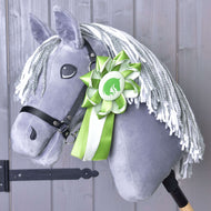 Hobby Horse Kokarda Zelená NEW od Hobby Horse LarDen s šedým plyšem, bílou přízovou hřívou, černou uzdečkou a zelenobílou kokardou připnutou na krku, zobrazený na dřevěném pozadí.