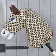 Hobby Horse ochranný oblek Luxus Design od Hobby Horse LarDen s černobéžovou vzorovanou hlavou, plstěnýma ušima, našitým okem, bílým čenichem a pratelnými materiály, nasazený na dřevěné tyči před šedou stěnou.