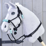 Provazový set Turquoise od Hobby Horse LarDen je zobrazen na šedém plyšovém Hobby Horse s bílou hřívou, černou uzdečkou a tyrkysovými detaily, upevněném na dřevěné tyči před šedou dřevěnou stěnou.