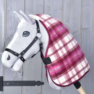 Šedý hračkový Hobby Horse s černou uzdečkou má přes krk červeno-bíle kostkovanou Deka stájová LarDen od Hobby Horse LarDen. V pozadí je dřevěná stěna se svislými prkny.