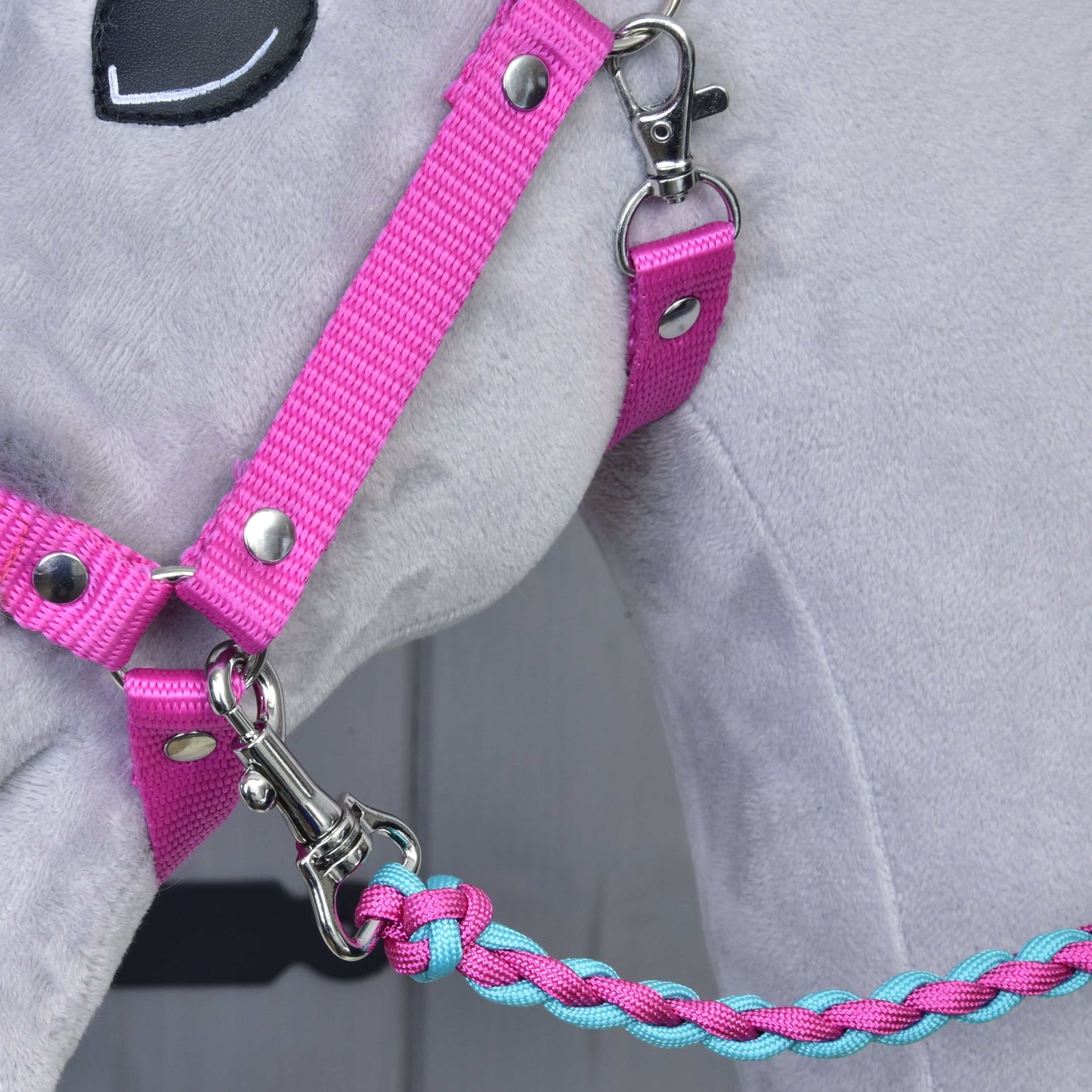Detailní záběr na šedého plyšového koně se Set Perfect Combination Pink od Hobby Horse LarDen – růžová ohlávka s kožešinovým polstrováním s pleteným modro-růžovým vodítkem, připevněným stříbrnou karabinou – ideální pro fanoušky doplňků pro hobby horse.