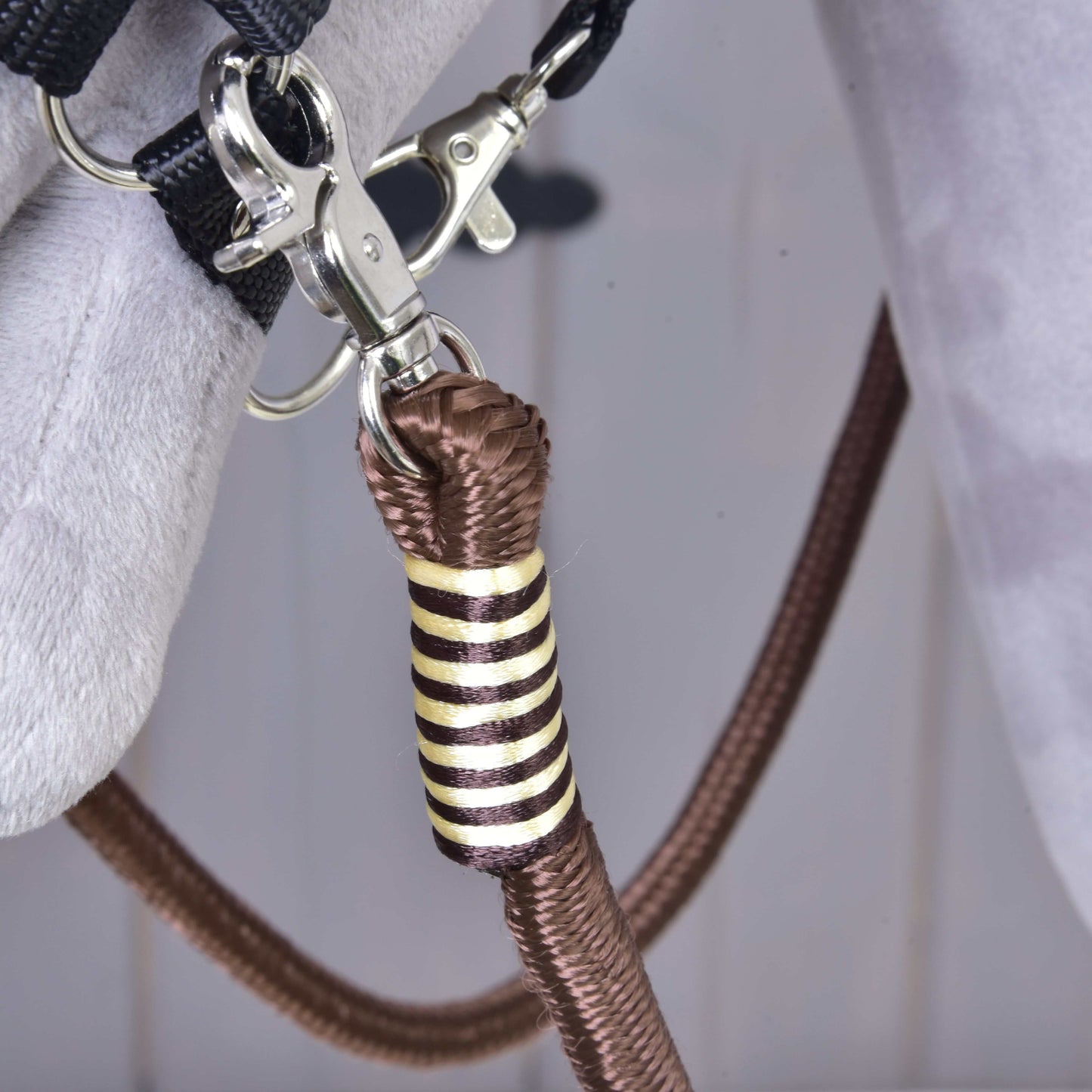 Detail kovové karabiny připevňující hnědé polypropylenové lano se zlatým a černým ozdobným omotáním k šedé látce, součást Otěží Vivaldi od Hobby Horse LarDen.