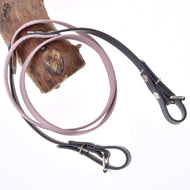 Otěže pogumované Dark Grey/pink od Hobby Horse LarDen dvakrát omotané kolem světle hnědé dřevěné větve, připomínající kožená vodítka pro psy, na bílém pozadí.